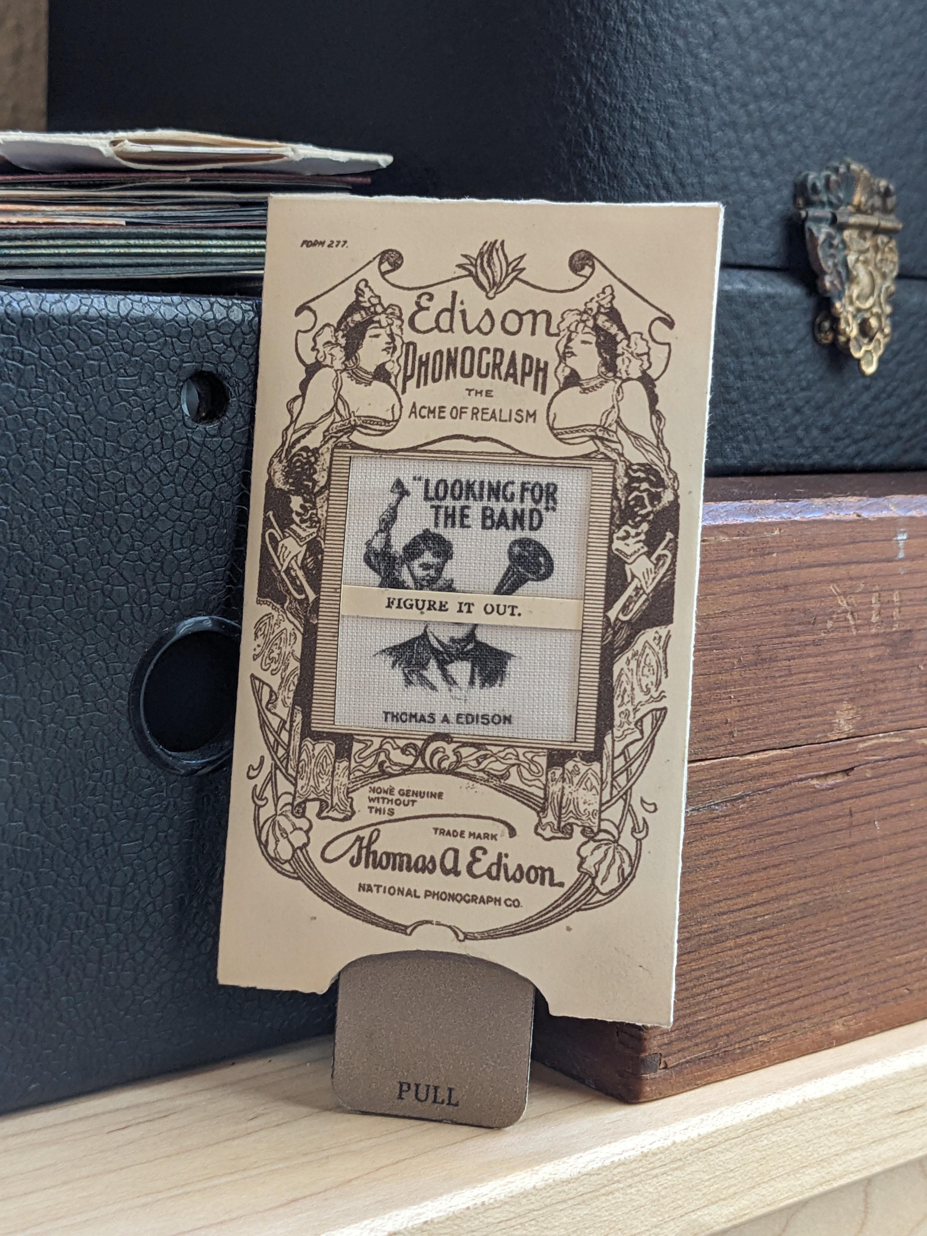 A photograph of a handheld novelty with a pull tab adertising the Edison Phonograph